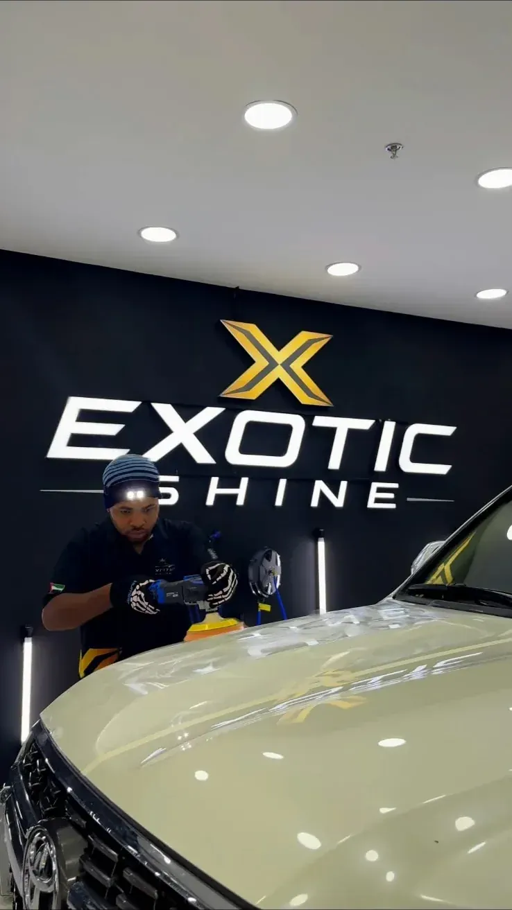 A technician machine-polishing a bonnet under the Exotic Shine sign